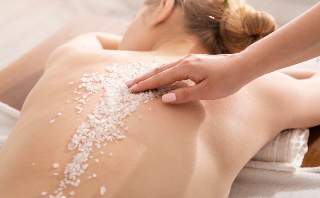 Hands applying exfoliating salt on woman back